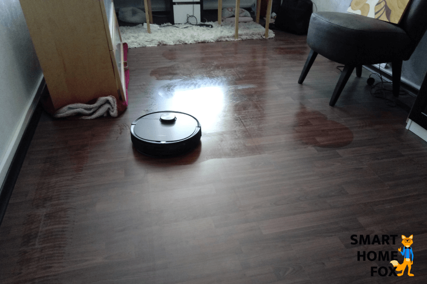 Man sieht, wie ein Saug-Wischroboter den Holzfußboden wischt. 